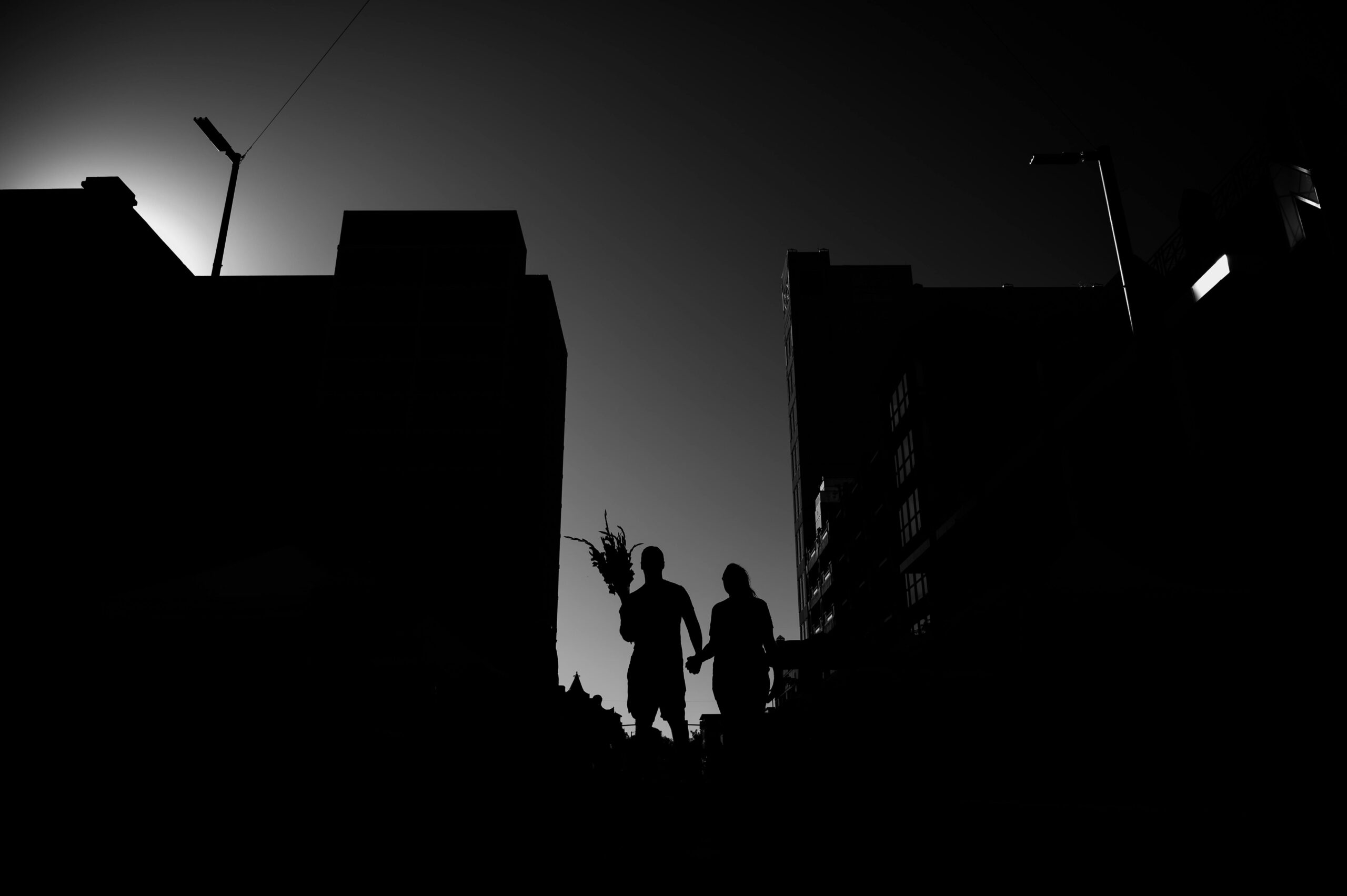Silhouette of a couple holding hands in an urban setting during sunset.